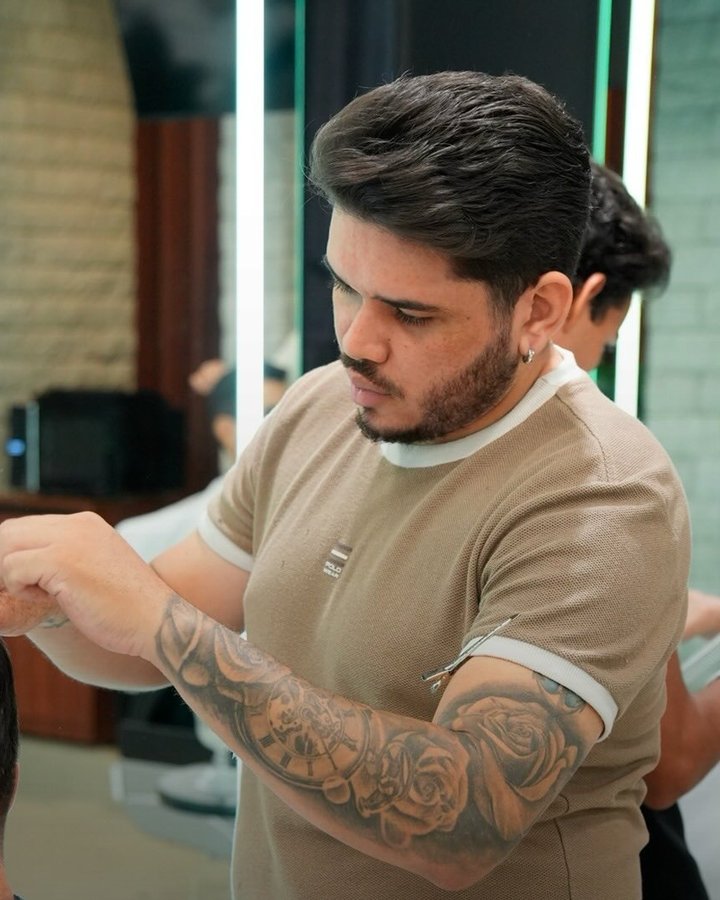 Barbeiro tatuado cortando com tesoura e pente