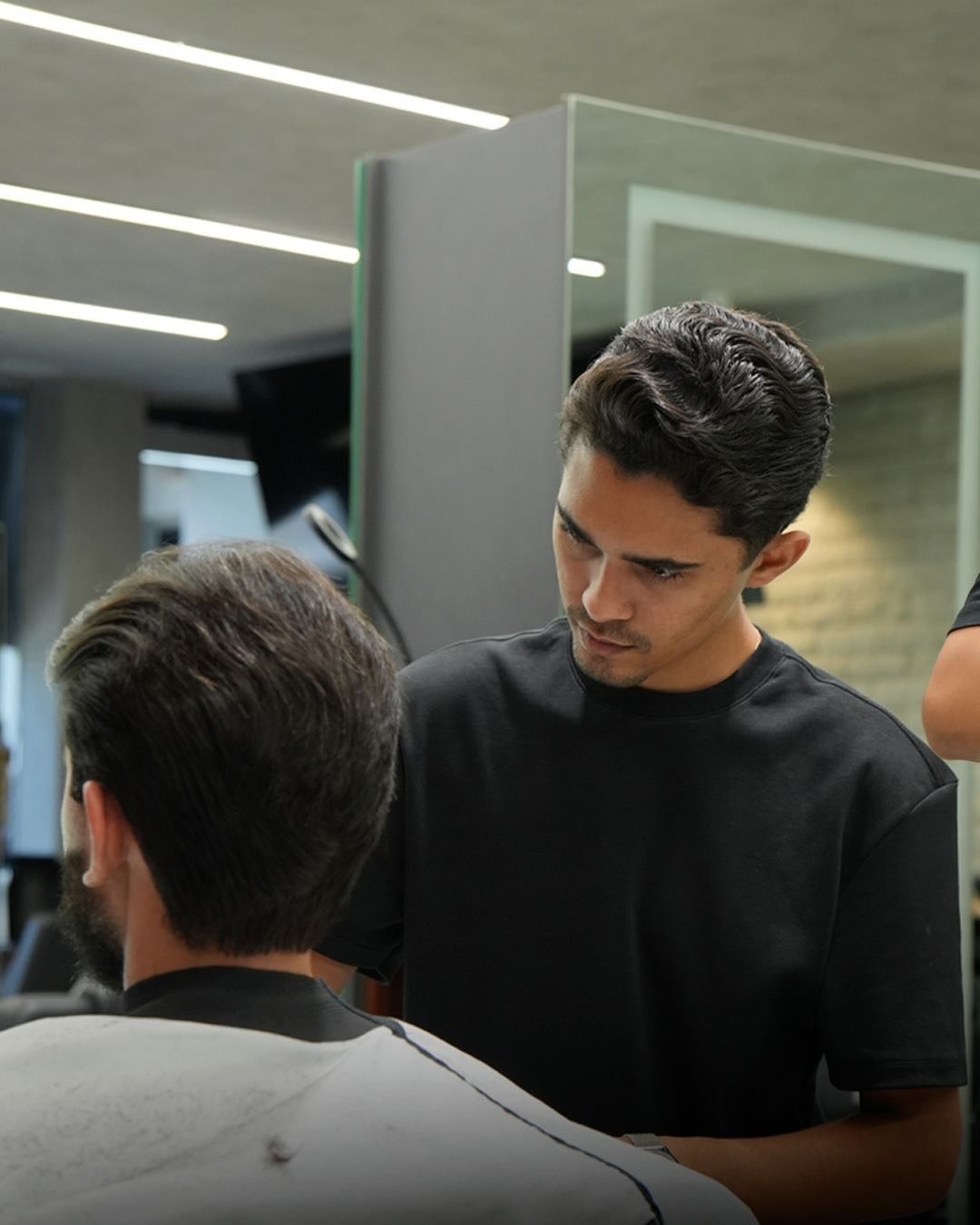 Barbeiro da Bozzi concentrado no corte, diante do espelho iluminado